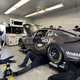 A block Chevrolet Camaro stock car on stands as the crew work on the car.